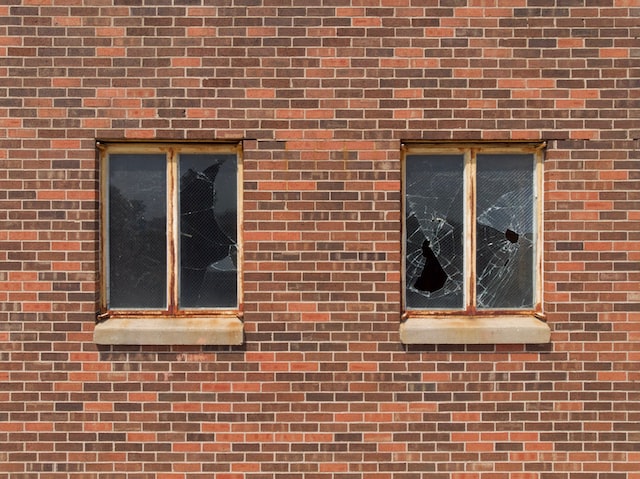 two windows on a brick building with one of them being badly shattered